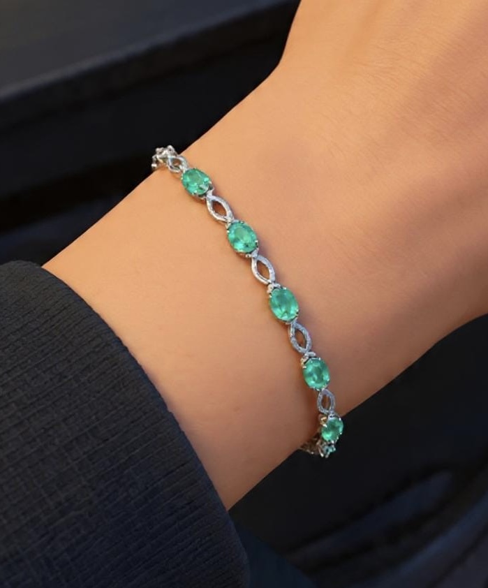 Link bracelet with oval-cut green gemstones in white metal, worn on a wrist